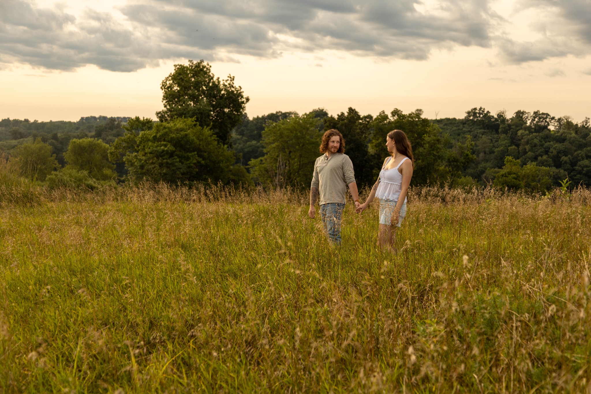 Couple holding hands in a wide field beneath a dramatic sky